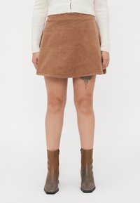 Bruine corduroy mini-rok met diagonale stikdetails, gecombineerd met stijlvolle bruine enkellaarsjes. De rok heeft een uitlopende vorm en een gestructureerde stof.