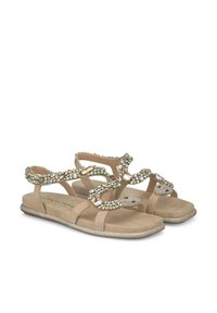 Sandalias beige con una suave textura de ante, que presentan detalles decorativos de cristales y un diseño serpentino en las correas. Suela plana con brillo.