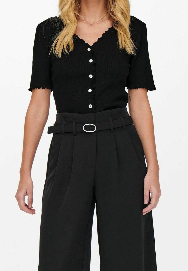 Black ribbed knit top with short sleeves and scalloped edges, featuring a row of light buttons. Paired with high-waisted black trousers and a belt.