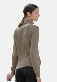 Pull beige avec un col montant, doté d'un motif en losanges texturé et de poignets et d'un ourlet côtelés. Porté avec un jean noir.