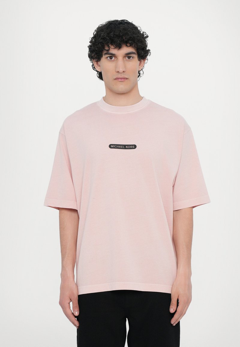 T-shirt oversized rosa claro feita de algodão, com decote redondo e mangas curtas, apresentando um patch de logotipo preto ao centro.