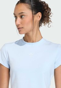 Svetlomodré športové tričko s okrúhlym výstrihom, krátkymi rukávmi a vyšitou bielou logom Adidas na hrudi. Mäkká textúra látky.