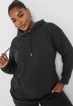Mustahiila t-shirt mweusi wa ribbed ulio na mtindo wa uhuru, mikono mirefu, na nyuzi zinazoweza kubadilishwa. Nyenzo laini yenye mapambo ya vifaa vya fedha.
