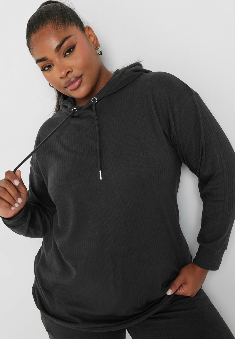 Mustahiila t-shirt mweusi wa ribbed ulio na mtindo wa uhuru, mikono mirefu, na nyuzi zinazoweza kubadilishwa. Nyenzo laini yenye mapambo ya vifaa vya fedha.
