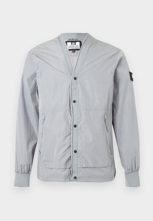 Jachetă ușoară pentru bărbați, de culoare gri deschis, cu nasturi tip capse, buzunare laterale cu fermoar, manșete striate și o emblemă neagră pe mâneca stângă.