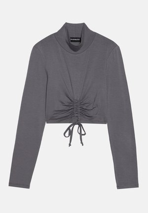 Maglia grigia a maniche lunghe e cropped con collo alto. Presenta dettagli arricciati con lacci regolabili all'orlo per un aspetto aderente.