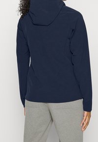 Navy blue, hooded long-sleeve jacket with soft fabric, fitted design, and seam detailing. Paired with light gray sweats visible at the waist.