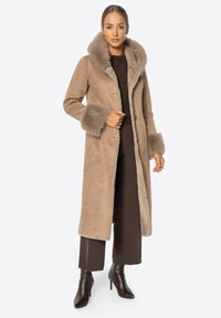 Beżowy długi płaszcz z sztucznym futrem na kapture i mankietach, wykonany z miękkiego zamszu, o prostym kroju z guzikami z przodu.