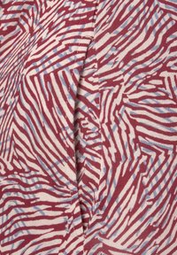 Κόκκινο και μπλε αφηρημένο μοτίβο σε ανοιχτό ύφασμα, με κυματιστές γραμμές και υφή, με ορατή ραφή και λεπτομέρεια ραφής.