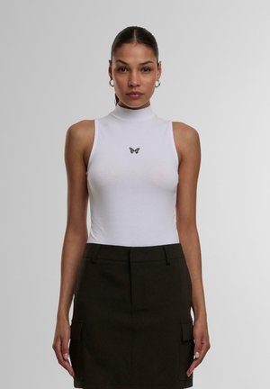 Hvid ærmeløs bodysuit med høj krave; har små sorte sommerfuglebroderier på brystet. Model bærer en mørkegrøn nederdel.