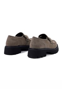 Scarpe in suede marrone con una spessa suola in gomma nera, caratterizzate da una punta arrotondata e hardware decorativo sul lato.