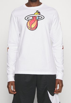 Homme portant un t-shirt blanc à manches longues avec un logo coloré de basket-ball enflammé et un short de sport noir avec un motif swoosh blanc.