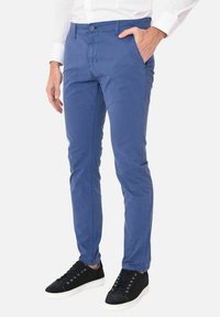 Chinos in cotone blu con vestibilità dritta, fronte piatto e chiusura con bottone. Abbinati a sneaker nere con suole e lacci bianchi.