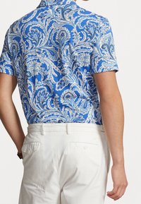 Kortärmad skjorta med blå och vit paisleymönster, med en knapp-down krage. Matchas med vita byxor för en avslappnad look.