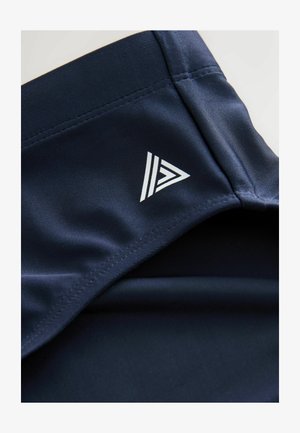 Sügavsinised sportlikud lühikesed püksid, mida iseloomustab sile tekstuur, valge kolmnurkne logo ja puhtad õmblused.