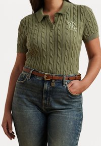 Olivově zelené pletené polo s textura kabelem, krátké rukávy a límcem. Spárováno s modrými džíny s vysokým pasem a hnědým páskem.