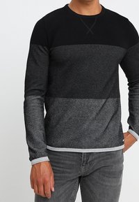 Maglia a maniche lunghe nera e grigia con motivo a maglia lavorata, scollo rotondo e polsini a contrasto. Gli orli sono rifiniti con una bordatura grigia.