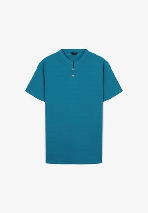 Chemise turquoise à manches courtes avec un col mandarin, ornée de trois boutons au niveau du décolleté et d'un tissu texturé.