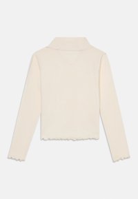 Top a maniche lunghe beige chiaro con texture a coste, design cropped e bordi ondulati lungo l'orlo e i polsini, dotato di un colletto.