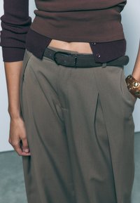 Rjav rebrast pulover v kombinaciji z visokim pasom, zmanjkanimi olivno zelenimi hlačami. Obleka vključuje temen pas in zlat zapestni trak.