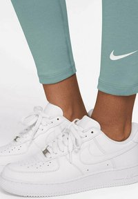 Gröna träningsleggings med slim fit och mudd vid anklarna med en vit Nike-logotyp. I kombination med vita läder Nike Air Force 1 sneakers.