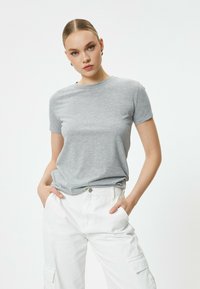 Grå T-shirt med korte ærmer og broderet "vær ikke ensom" besked på forsiden, kombineret med hvide cargo bukser. Glat tekstur.
