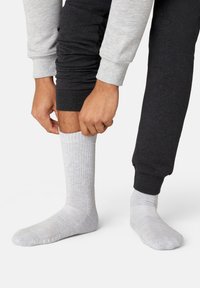Light grey ribbed sock being pulled on over dark grey sweatpants. The sock features a textured knit pattern and soft material.