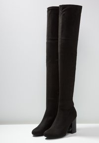 Bottes noires montantes au-dessus du genou en daim, dotées d'un talon épais, d'un bout arrondi et d'une fermeture éclair latérale. Texture lisse, sans motifs visibles.