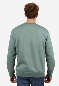 Sudadera verde con cuello redondo y puños acanalados, hecha de un material suave. Presenta un diseño liso sin patrones visibles.