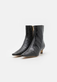 Bottes noires en cuir à la cheville avec une texture crocodile, bout pointu et détail de fermeture éclair dorée, avec un talon bas et arrondi.