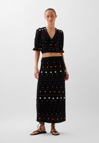 Ensemble en tricot noir en deux pièces comprenant un haut court à manches ballon et une longue jupe, ornée de motifs floraux colorés et d'accents.