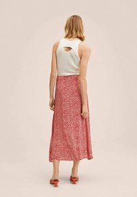 Débardeur blanc avec une découpe au dos, associé à une jupe longue rouge à fleurs. Tissu lisse, longueur chevilles, avec de petits motifs de fleurs blanches.