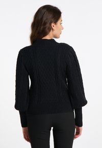Pulover negru tricotat, cu un design de cablu texturat, guler înalt, mâneci puff și tiv rib. Materialul pare moale și gros.