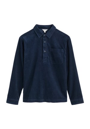 Tumši zila korduroja garām piedurknēm krekls ar apkakli, trīs pogu aizdari un krūšu kabatu. Iezīmējas ar ribotām tekstūrām un taisnu apakšmali.