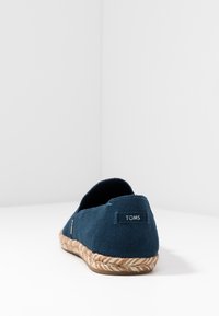 Zapato sin cordones de ante azul marino con suela de cuerda de yute. Presenta una pequeña etiqueta de TOMS en la parte trasera. Diseño de punta redonda.
