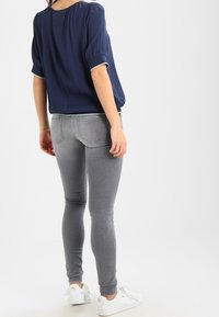 Tmavě modrá blůza s krátkým rukávem a nařasenými rukávy v kombinaci se světlými šedými skinny džíny. Bílé tenisky dokreslují vzhled.