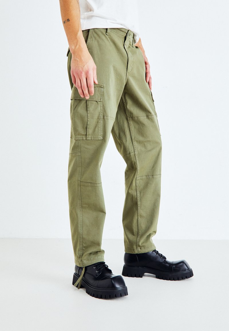 Pantaloni cargo verde oliva con multiple tasche, design a gamba dritta, materiale in cotone e cuciture rinforzate; abbinati a scarpe platform nere e chunky.