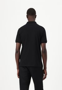 Μαύρο πόλο μπλουζάκι από απαλό βαμβάκι, με κλασικό γιακά, κοντά μανίκια και πλαϊνές σχισμές για ευκολία κινήσεων.