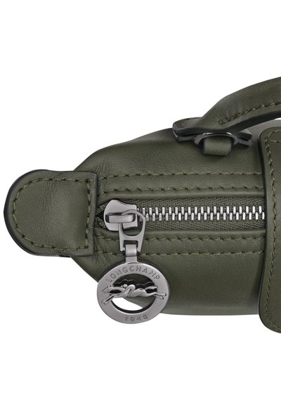 Olive green leather bag with a textured finish, featuring a silver zip closure and a circular metal logo tag. Smooth accents and stitching details.