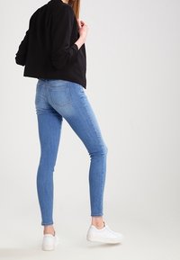 Modré úzké džíny z denimu se středním pasem, předvedené s černou krátkou bundou a bílými teniskami.