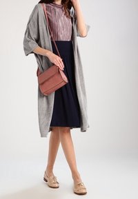 Woman wearing a gray open cardigan, pink striped blouse, navy skirt, beige loafers, and carrying a brown crossbody bag.