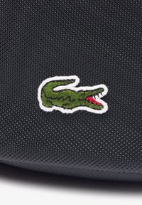 Logo de crocodile vert brodé avec des détails rouges sur un fond en tissu noir texturé.