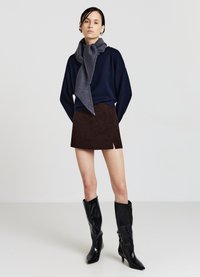 Marineblauer Pullover, grauer Strickschal, brauner Cord-Minirock und kniehohe schwarze Lacklederstiefel mit spitzer Zehe. Minimalistisches Design.