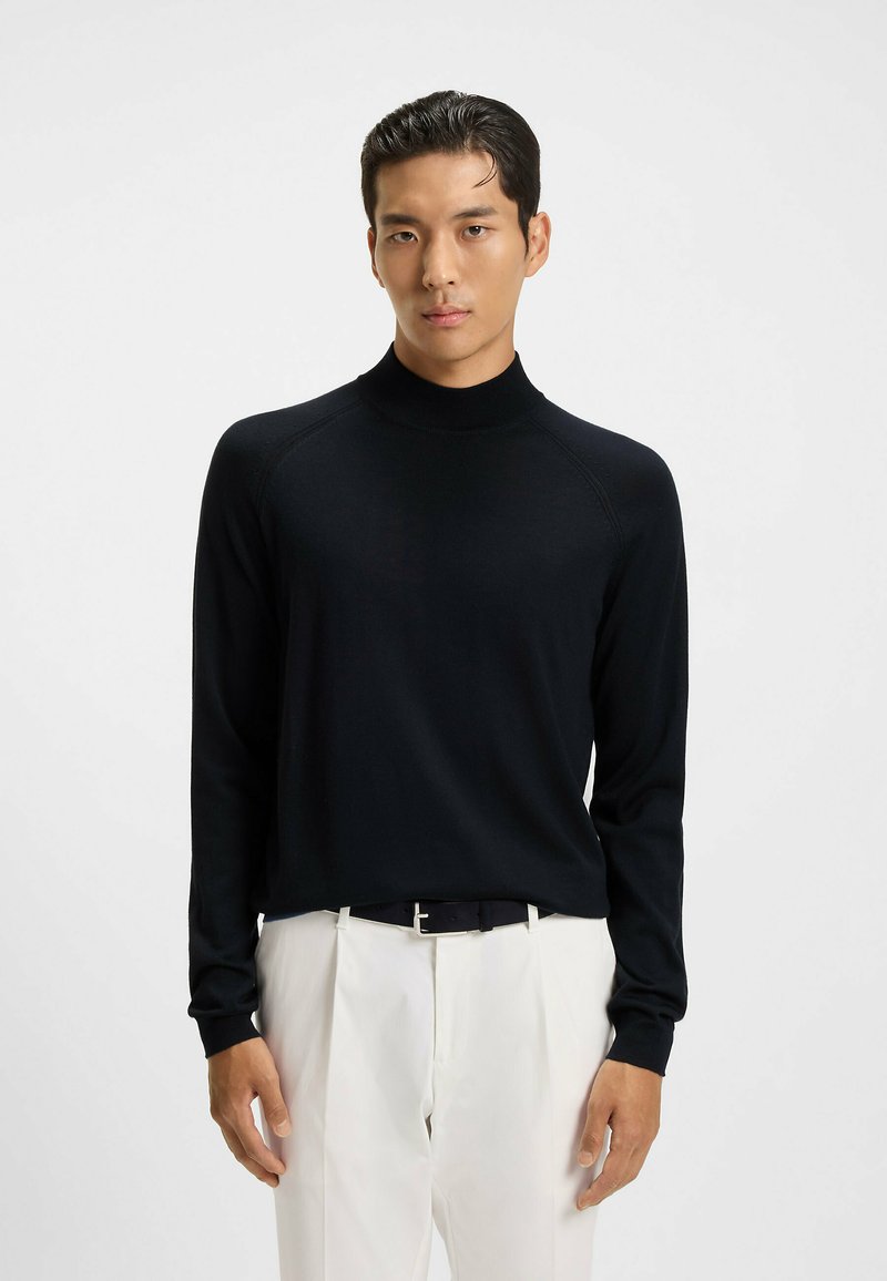 Maglione nero a collo alto in un filato leggero, con maniche lunghe e design aderente, abbinato a pantaloni chiari.