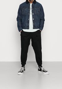 Jeansjacka med svart fleecekrage, ljusblå t-shirt och svarta cargojoggers med elastiska muddar, tillsammans med svarta högstövlar.