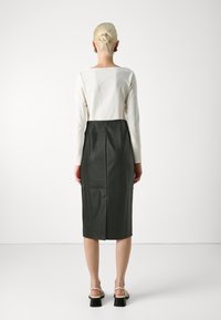 Vestido midi de cuero verde oscuro con un diseño ajustado, que presenta una parte superior beige en contraste y una costura central en la parte posterior, visto desde la vista trasera.