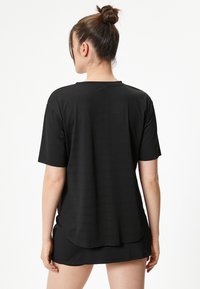 Camiseta negra de manga corta con un ajuste holgado, que presenta un cuello redondo y un tejido texturizado. Detalle de dobladillo trasero ligeramente más largo.