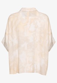 Ljus beige kortärmad blus i mjukt tyg, med ett subtilt tie-dye mönster, lös passform och en slits i nackpartiet bak för ventilation.