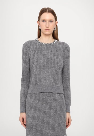Grauer, gestrickter Pullover mit langen Ärmeln, einem strukturierten Muster und einem silbernen Kettensaum um den Kragen. Kombiniert mit einem passenden grauen Rock.