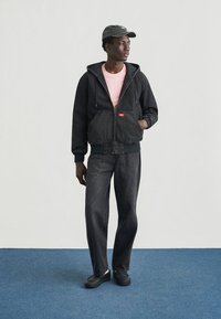 Μαύρο τζιν μπουφάν με κουκούλα, ροζ μπλούζα και τζιν παντελόνι σε μαύρο χρώμα που ταιριάζει. Μαύρο καπέλο και παπούτσια ολοκληρώνουν το σύνολο. Λείο υλικό, casual σχεδιασμός.